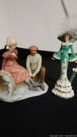 Two figurines together: ice skating couple and woman in green dress with feathered hat