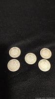 Five silver dimes arranged on black surface showing the coin inscriptions and dates.