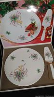Top view of boxed cake plate with Christmas ribbon and holly design and matching ceramic cake lifter tied with gold cord, displayed in presentation box.