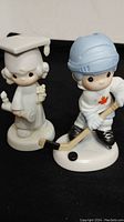 Photo of two Precious Moments figurines: graduation girl and hockey player boy.