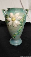 Front, full view of 10-inch Roseville vase featuring floral relief design and two handles on a black background.