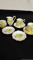 Full set arranged showing two demitasse cups with saucers, cream pitcher, sugar bowl, and two pin dishes with yellow tea rose pattern.