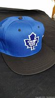 Front view of the blue and black snapback cap showing the Toronto Maple Leafs white embroidered logo on the front panel.