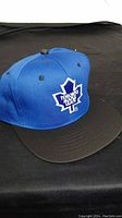 Blue snapback cap with Toronto Team maple leaf logo on front and black brim, placed on black background.