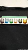 Set of six multicoloured short shot glasses in original box, displayed in a row showing the full set.