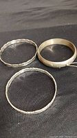 Three sterling silver vintage bangles on black cloth showing different textures and designs