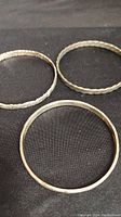 Three vintage sterling silver bangles laid flat on a dark surface showing different textures and designs.