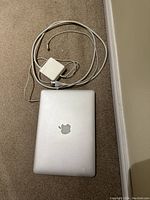 MacBook Pro closed on carpet with power supply charger with cable coiled beside it.