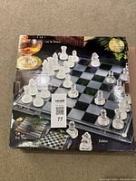 Packaged box showing image of transparent glass chess and checkers board with frosted and clear glass chess pieces arranged on it, labeled as a 3-in-1 game set including tric trac (backgammon), and echecs (chess).