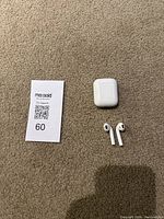 Photo of AirPods earbuds, charging case closed, and MaxSold lot tag on carpeted floor.