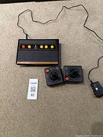 Atari Flashback 8 Gold console with two connected joystick controllers and visible power adapter cable laid on carpeted floor.