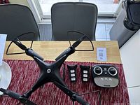 Holy Stone HS-100 drone placed on table next to remote control and two batteries.