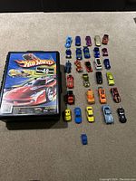 28 assorted Hot Wheels cars arranged in rows next to the black carrying case, showcasing different car styles and colors.
