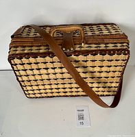 Side view of rectangular woven wicker picnic basket with leather strap and handle.