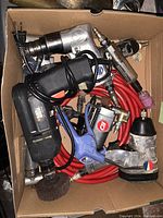 Box containing multiple drills and tools including pneumatic drills, electric drill, air hose, and air blow gun.