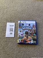 Front of PS5 game case titled Sackboy A Big Adventure placed on carpet next to MaxSold lot card number 56