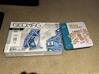 Closed boxes of Geomag Pro-L magnetic construction set and Solid Wood Brain Teasers tin box, showing packaging and titles.