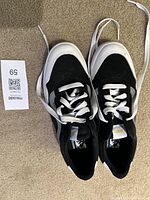 Top view of the black and white Vans men's shoes with white laces on carpeted floor showing size tag 9.5.