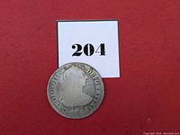 Side view with a number 204 on white card above coin on red background.
