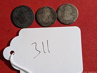 Three Spanish reale coins on a red background with a white tag numbered 311. Coins show wear and aging.