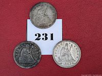 Three Seated Liberty silver quarters dated 1856 (two coins) and 1853 with arrows and rays, laid on a numbered card over red cloth. Shows obverse sides mostly.