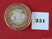 Obverse view of silver gaming token in plastic capsule alongside lot number card