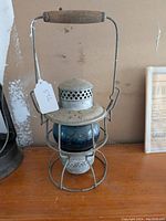 Front view of vintage lantern showing teal blue glass globe, wire protective cage and wooden handle.