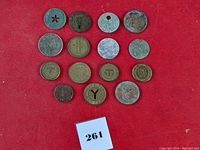 Overview showing 14 assorted metal tokens on red background, including tokens with star cutout, keyhole cutout, and various inscriptions.