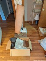 Rolled vegetable-tanned leather hide leaning against door with cardboard box and tool cases on floor