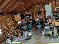 Wide view of garage floor showing assorted items: shelving, tables, air conditioner, vacuum, garbage bags