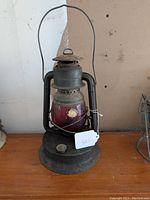 Full view of the Dietz Little Giant barn lantern showing ruby red glass globe, metal frame, and hanging handle.