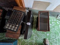 Five used wooden and glass front display boxes arranged on green patterned carpet; one has multiple round compartments for displaying small items.