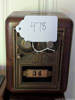 Front view of oak coin bank showing brass mailbox door with combination dials and number 34 label.