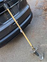 Full view of the stainless steel scoop with wooden handle placed against a car bumper.