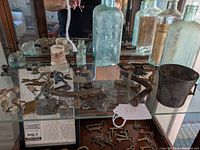 Display case view of the collection showing antique glass bottles, lead soldier figurines, metal artifacts including keys, a cup, and decorative metal items.
