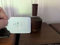 Side view of the vintage wooden butter mold on a wooden surface, showing the cylinder handle and body with a string tied around the handle.