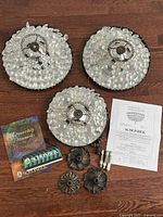 Three flushmount fixtures with crystals, canopy covers, hardware, documents laid on wood floor