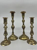 Four polished brass candlestick holders displayed in a row: two taller at about 10 inches and two shorter at about 7 inches.