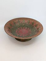 Angled side view showing shallow brass bowl with red and green inlay floral patterns and brass engraving.