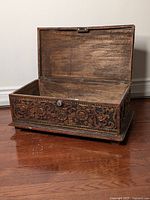 Open carved wooden chest showing detailed floral carvings and birds on the exterior with gold painted accents. Inside is unpainted wood.