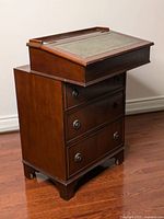Front angle view with closed hinged top, three drawers, bracket feet, leather inset top