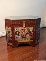 Front view of octagonal Burmese painted chest showing detailed cultural scenes and red/maroon base with gold accents.