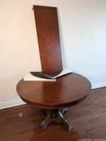 Round table with detached extension leaf and protective topper pieces leaning against wall