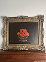 Full view of original oil painting in ornate frame showing red apples in glass bowl on dark background.