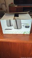 Box of Bose Companion 2.0 speakers showing front of packaging with image of speakers and control pod.