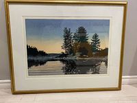 Framed landscape print showing a lakeside sunset with silhouetted trees reflected on water.