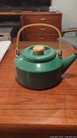 Side view of green kettle with wooden handle and knob, placed on wooden surface.