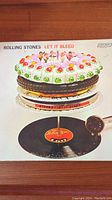 Front cover of The Rolling Stones "Let It Bleed" vinyl record sleeve showing detailed cake and record player artwork.