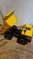 Side angle of the yellow and black vintage Tonka dump truck toy showing the raised dump bed and large tires.