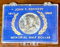 Top down view of the 1964 Kennedy Half Dollar obverse side inside protective case with blue insert and gold lettering.